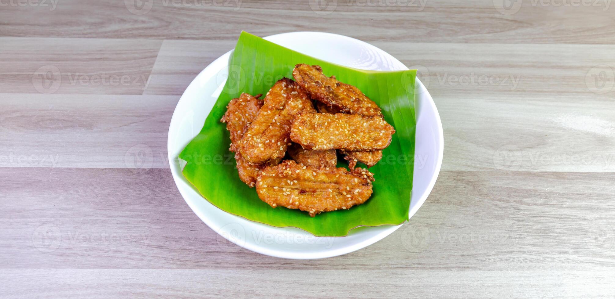 Crispy Thai fried bananas with sesame seeds served on a banana leaf in a white plate, Fried bananas is a traditional Asian snack with sweet, crunchy texture. Top view close-up shot, copy space photo
