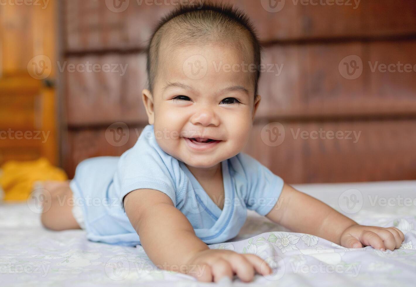 Happy Asian baby girl smiling and lying on his stomach on a bed at home, showing first teeth. Concept of childhood, innocence, and happiness photo
