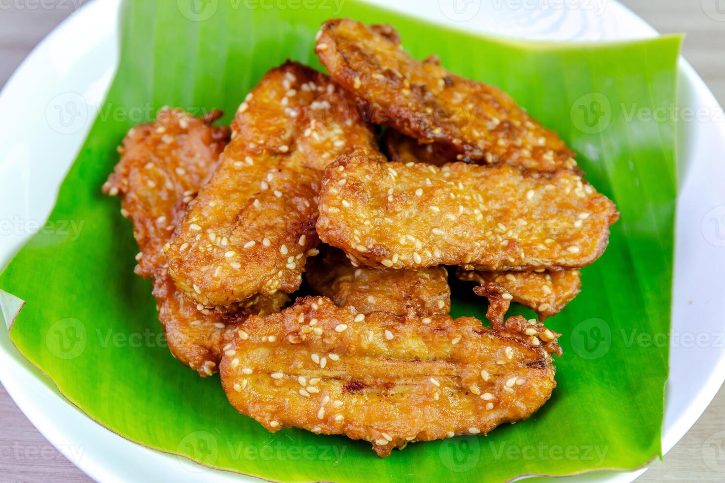 Crispy Thai fried bananas with sesame seeds served on a banana leaf in a white plate, Fried bananas is a traditional Asian snack with sweet, crunchy texture. Top view close-up shot photo