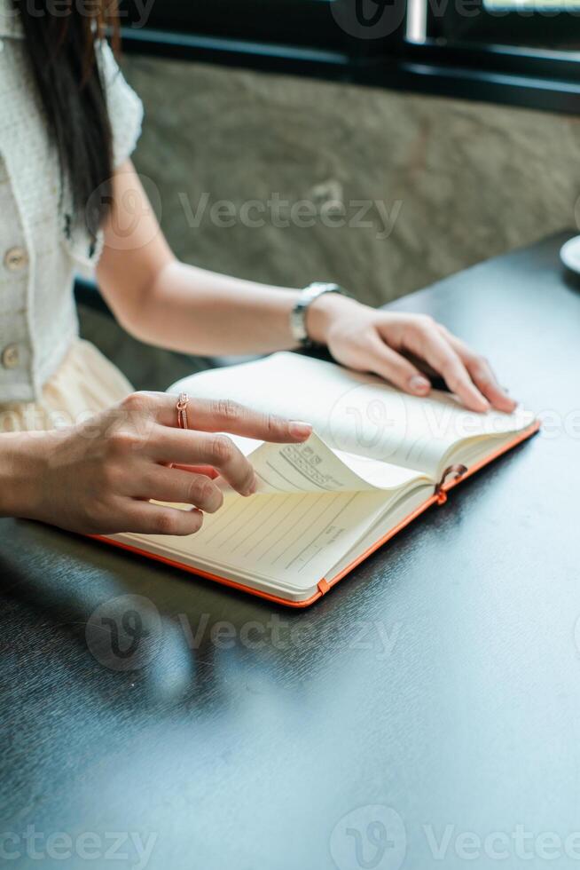 A woman turns pages of a notebook while seated at a desk, capturing a moment of focus and productivity. photo