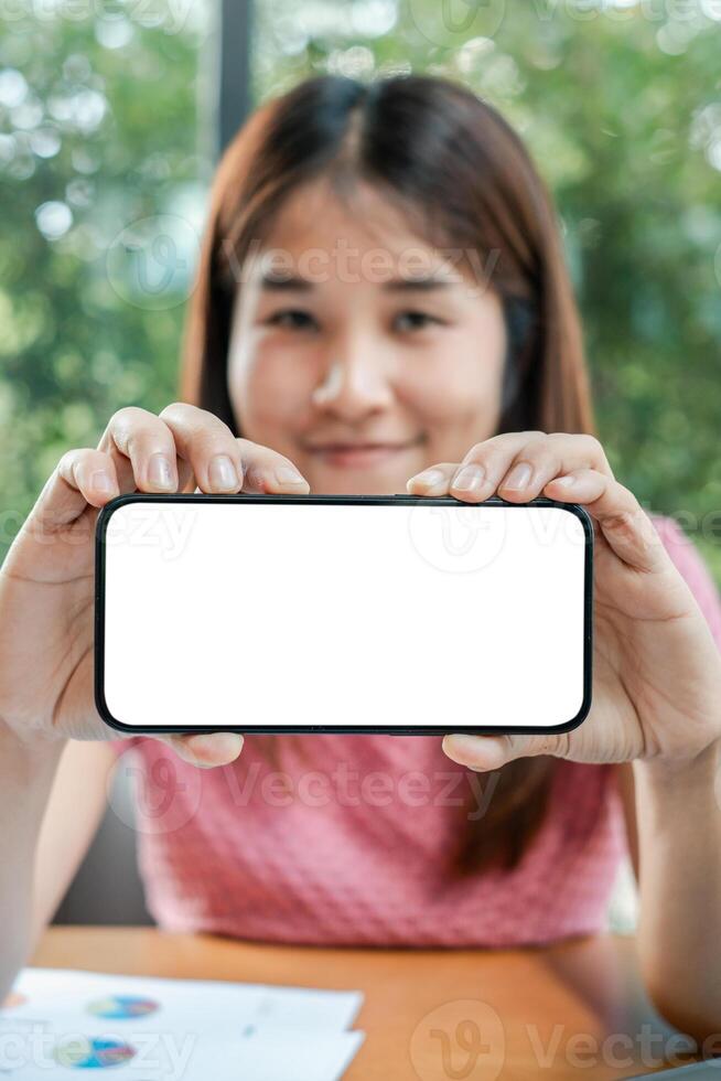 Woman displaying a smartphone with a blank screen, ideal for mockup or design purposes, in an office environment. photo