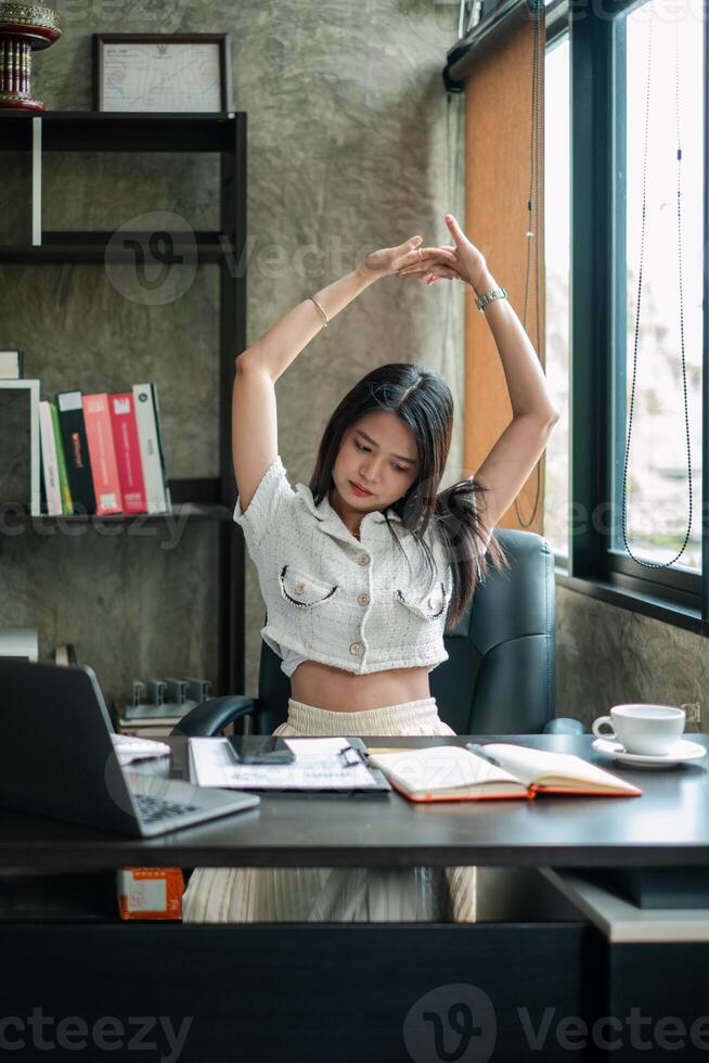 A young woman takes a break to stretch at her office desk, promoting wellness and productivity in a modern workspace. photo