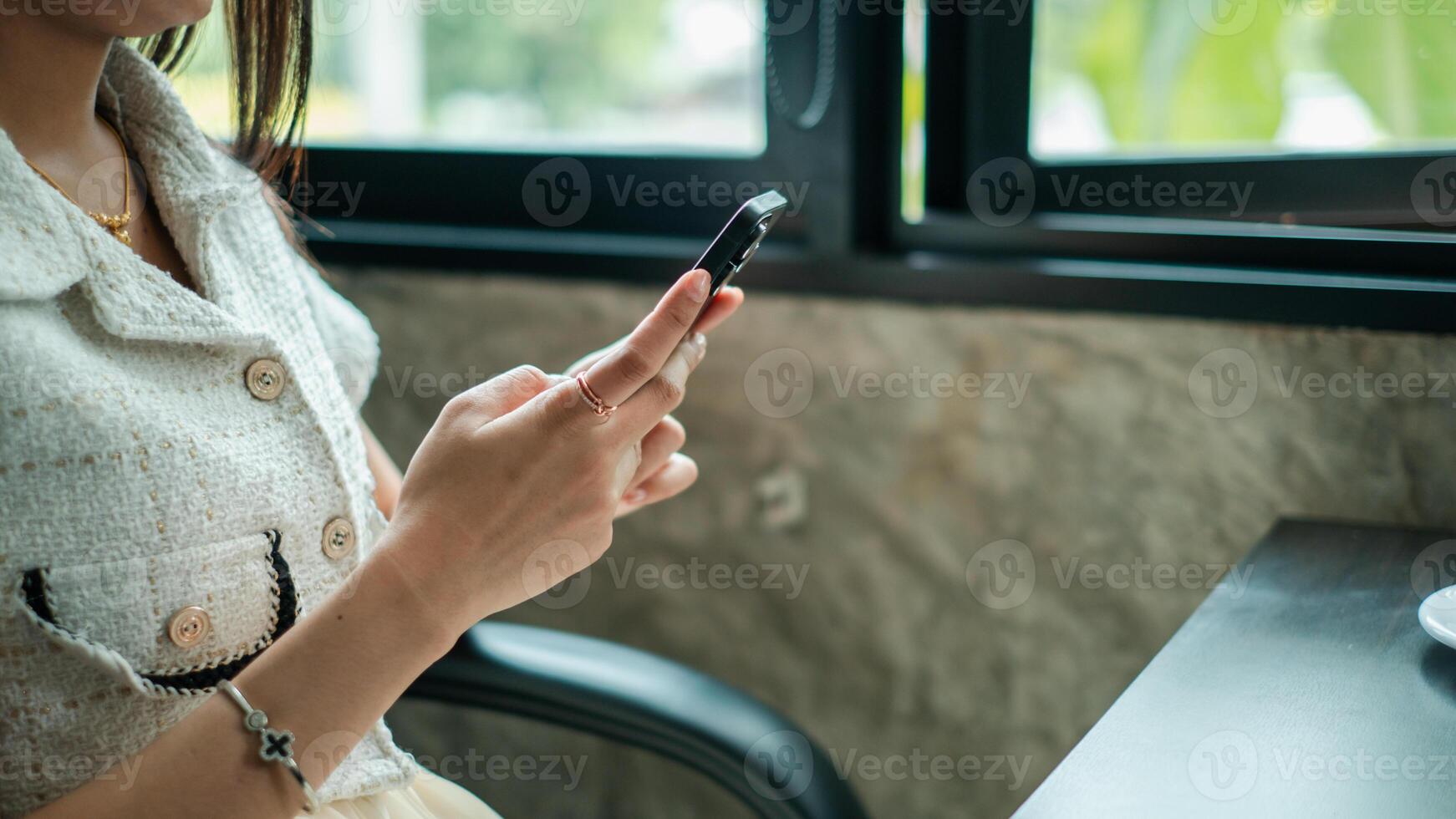 A woman sitting by a window in a cafe, using her smartphone, surrounded by natural light and modern decor. photo