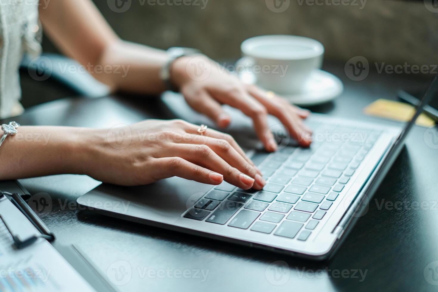 Hands typing on a laptop in a modern office environment with a coffee cup nearby, symbolizing productivity and technology. photo