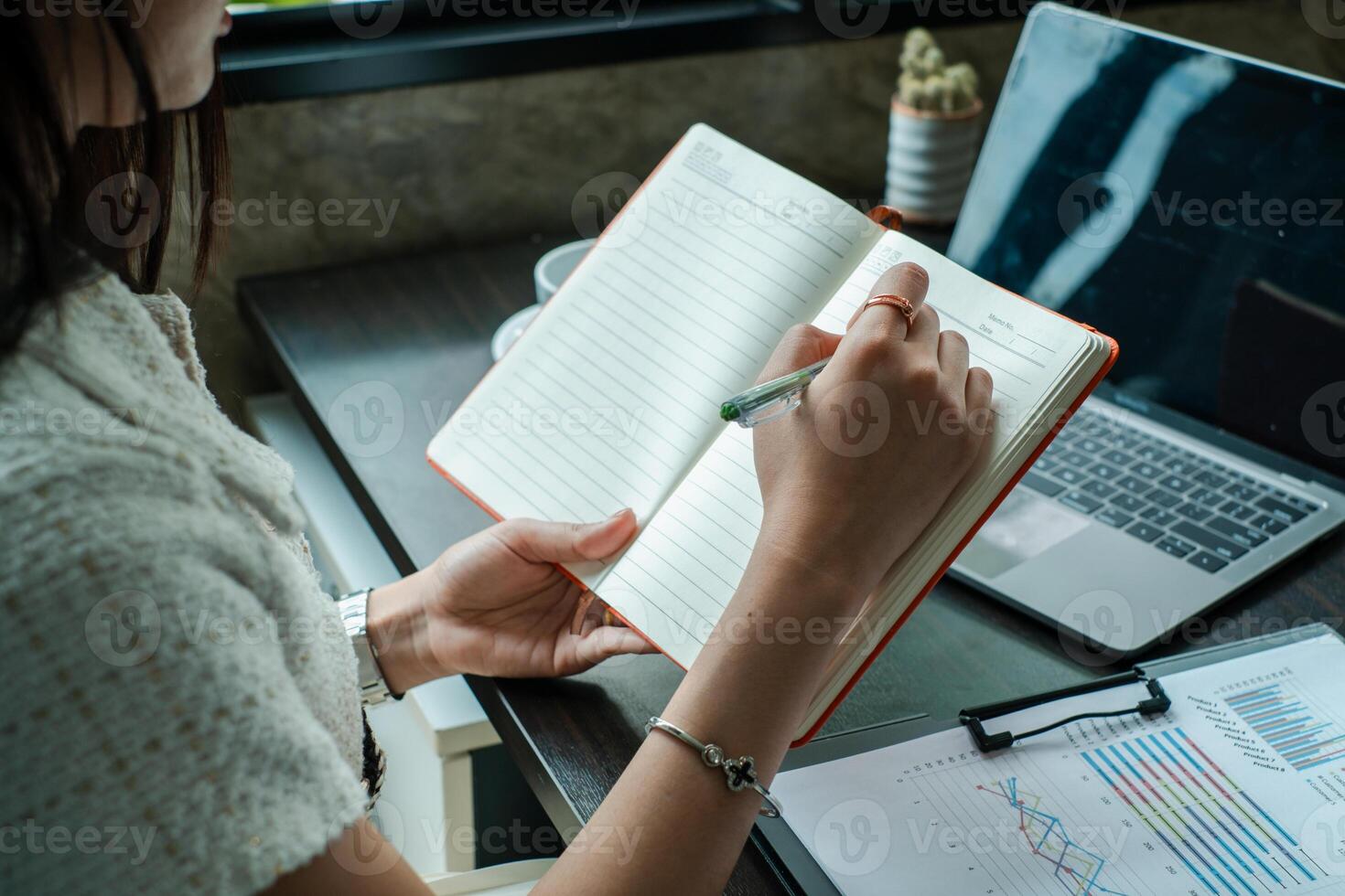 Professional woman taking notes at desk with laptop and financial documents, highlighting productivity and business planning. photo