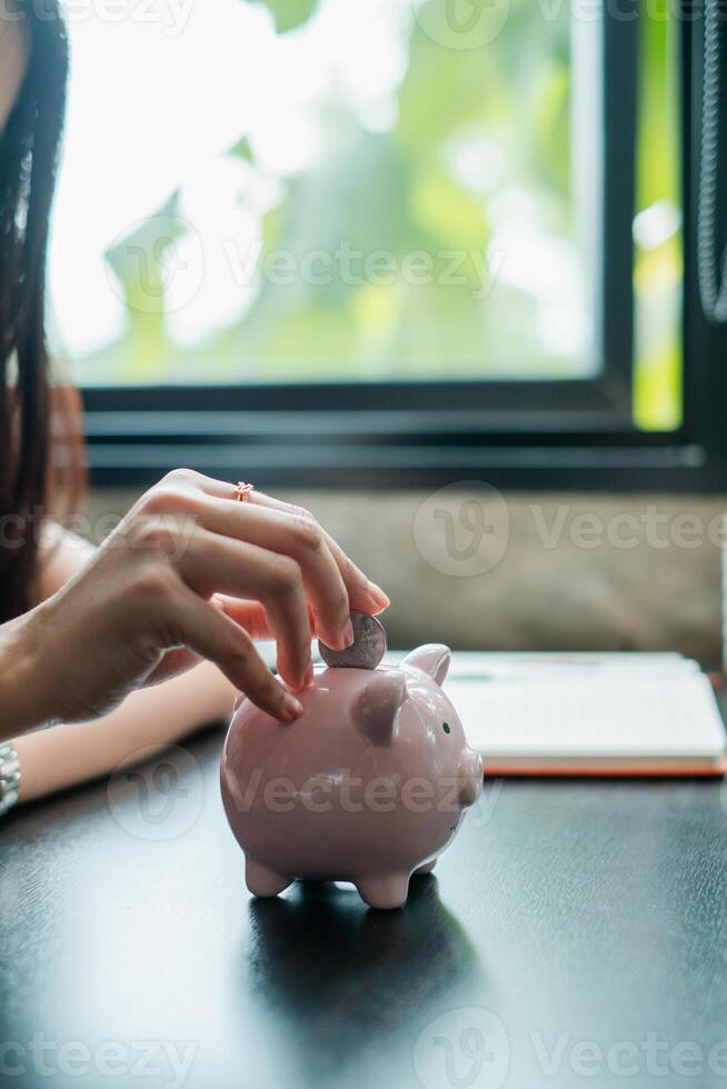 Close-up of a hand inserting a coin into a pink piggy bank, symbolizing savings and financial planning. photo