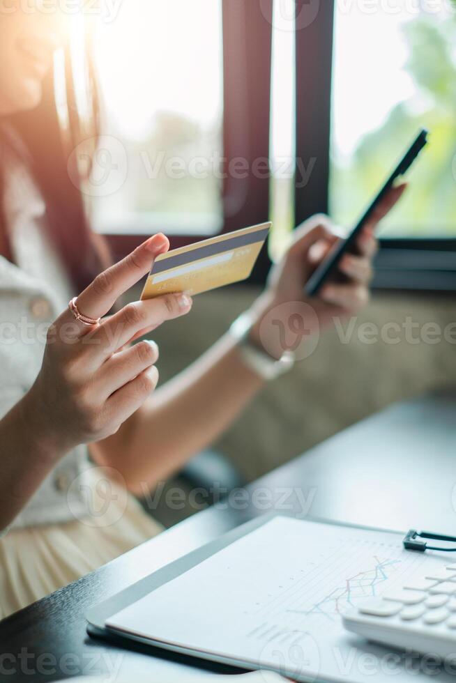 Close-up of a woman using a smartphone and credit card for online shopping in a sunlit office environment. photo