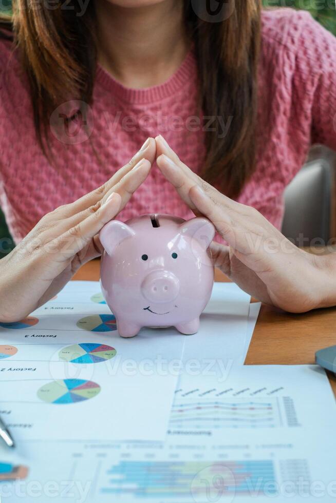Close-up of a woman shielding a piggy bank with hands, surrounded by financial documents and colorful charts. photo