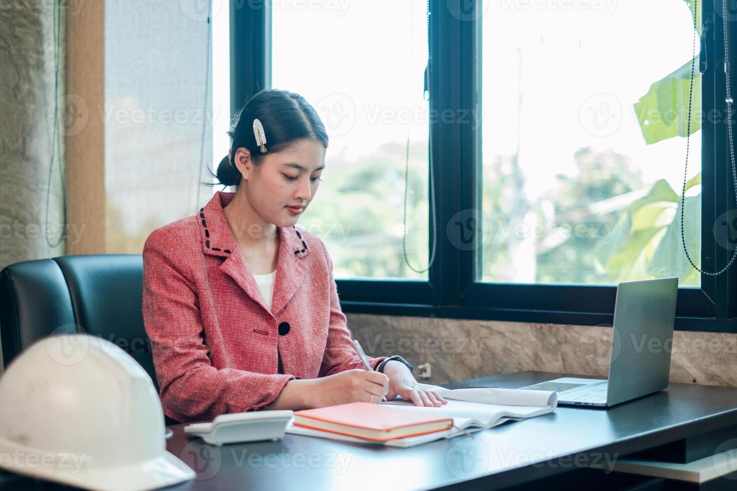Businesswoman in a pink blazer working at a desk with a laptop and documents, showcasing a professional office environment. photo