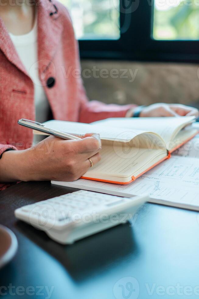 A business professional takes notes in a planner with a calculator on the desk, capturing a moment of productivity in a modern office. photo