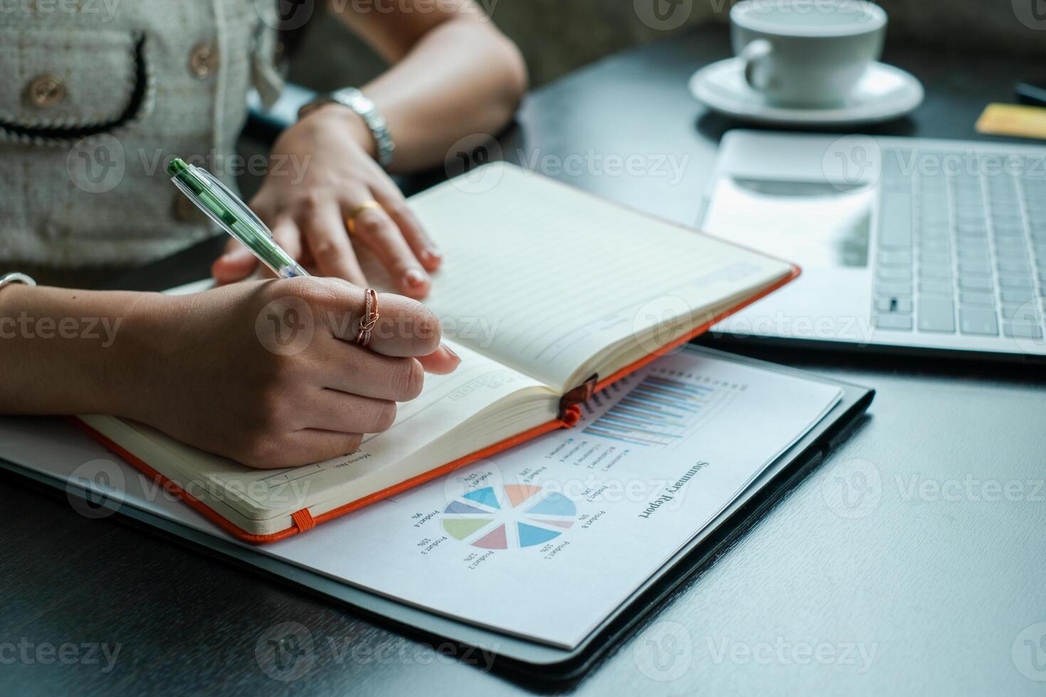 A business professional writing in a notebook while analyzing data on a laptop in a modern office environment. photo