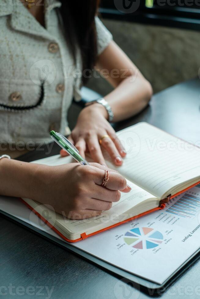 Professional woman taking notes in a notebook with financial charts on a desk, showcasing business and finance concepts. photo