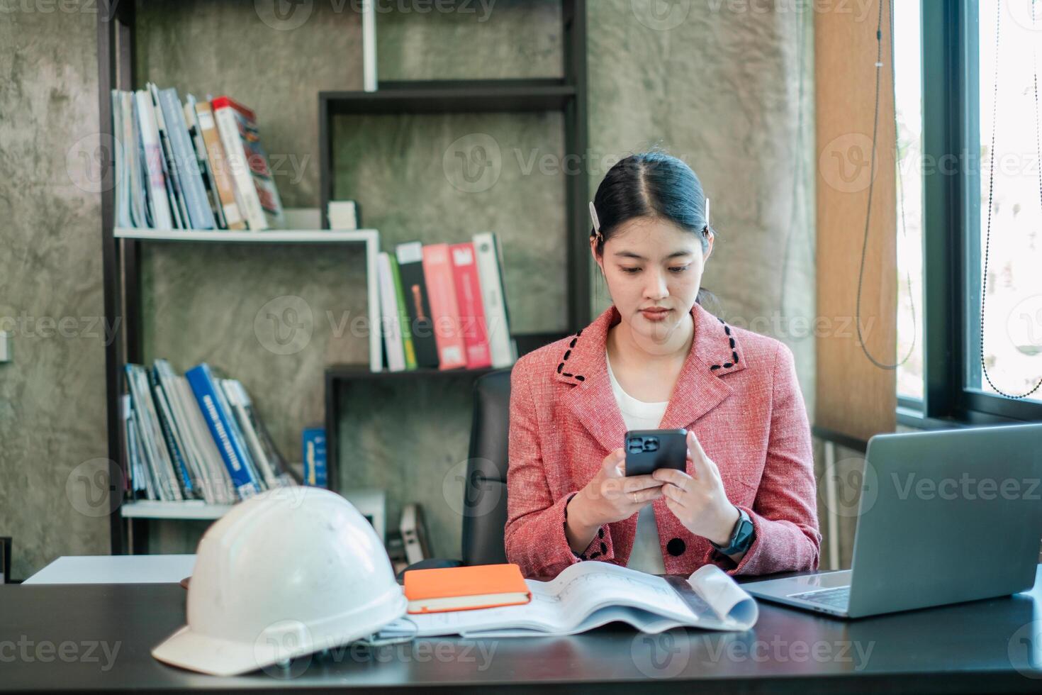 Businesswoman in a modern office using a smartphone, with a laptop and documents, showcasing a professional work environment. photo