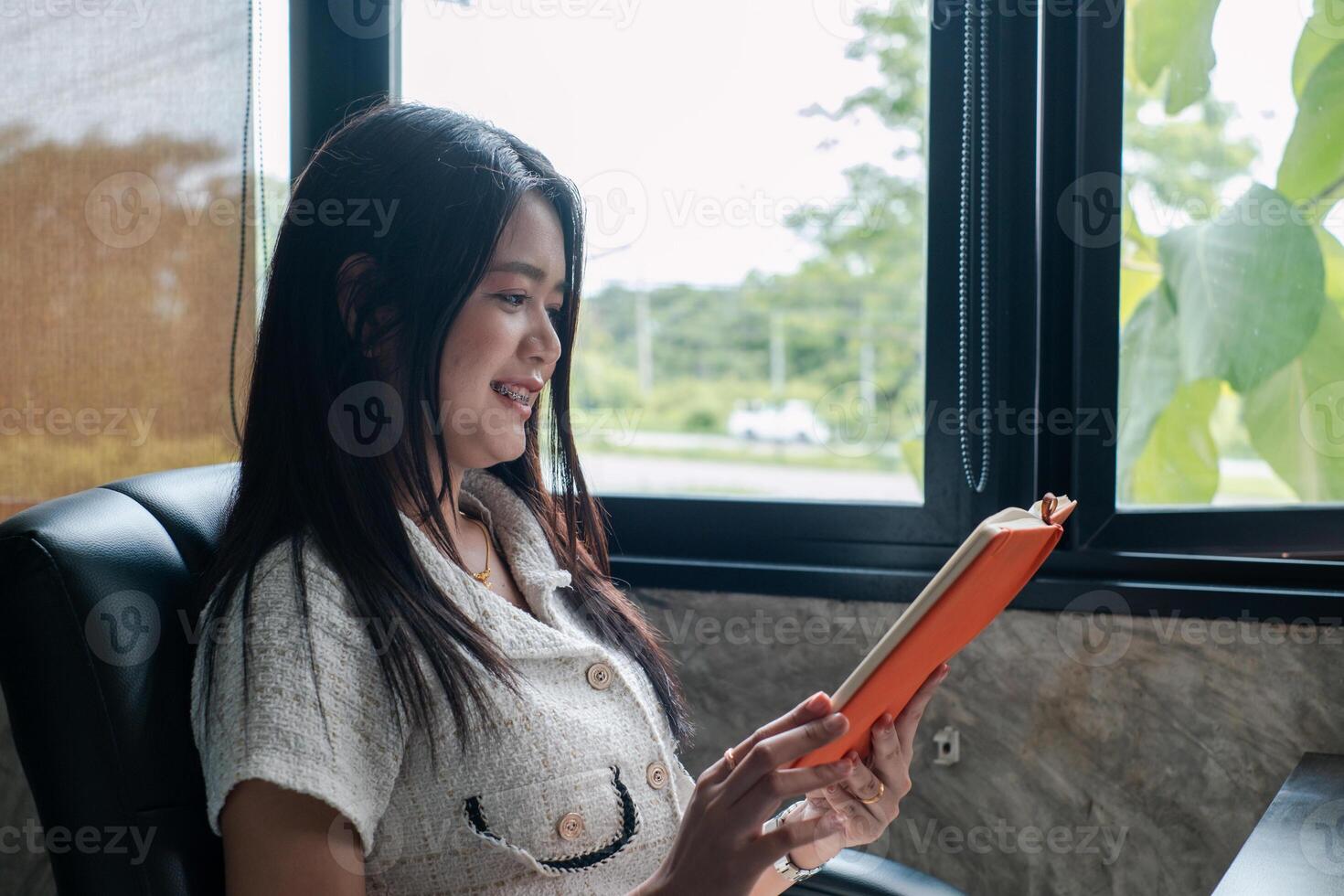 A woman sits comfortably by a window, reading a book, enjoying a peaceful moment in a cozy home environment. photo