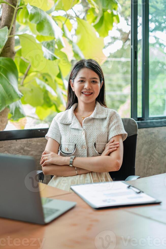 Young woman sitting confidently in a modern office with natural light and greenery in the background. photo
