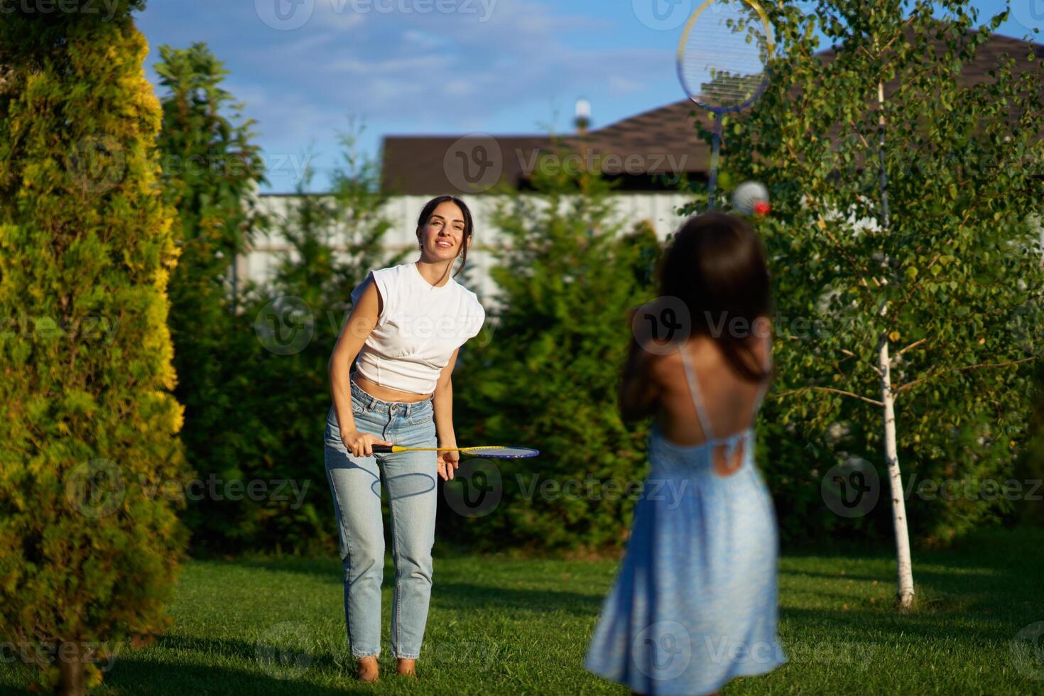 Woman and girl playing catch in a sunny backyard during late afternoon photo