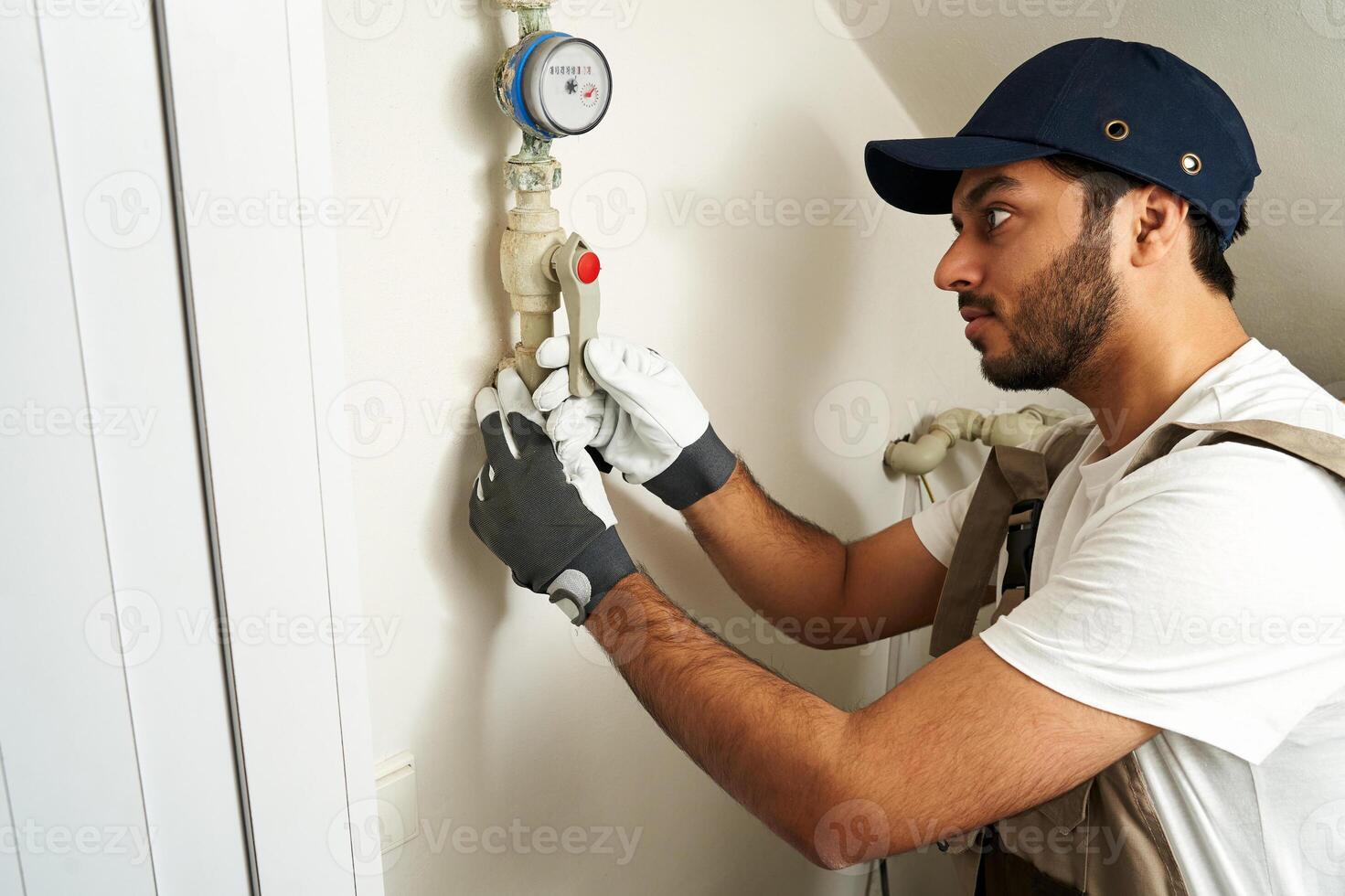 Professional male plumber in uniform is fixing water meter with special work tools at home photo