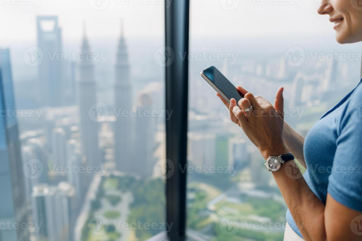 A Woman Engaged with Her Smartphone While Overlooking a Stunning Metropolis Skyline photo