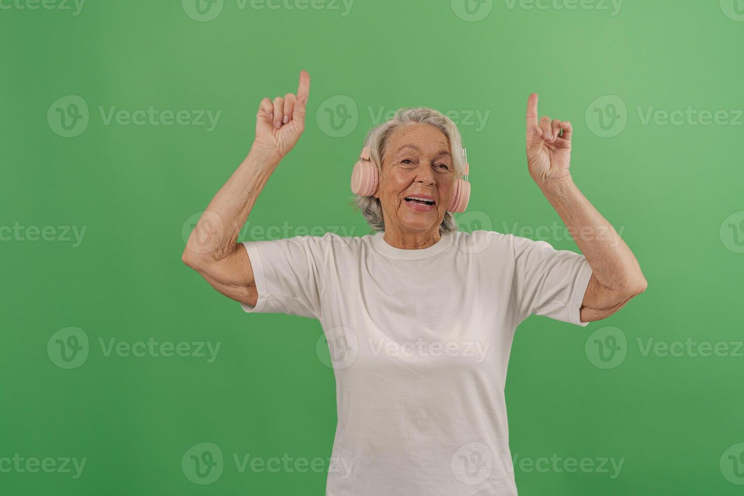 A Joyful Senior Woman is Dancing Happily with Earmuffs on a Bright Green Background photo