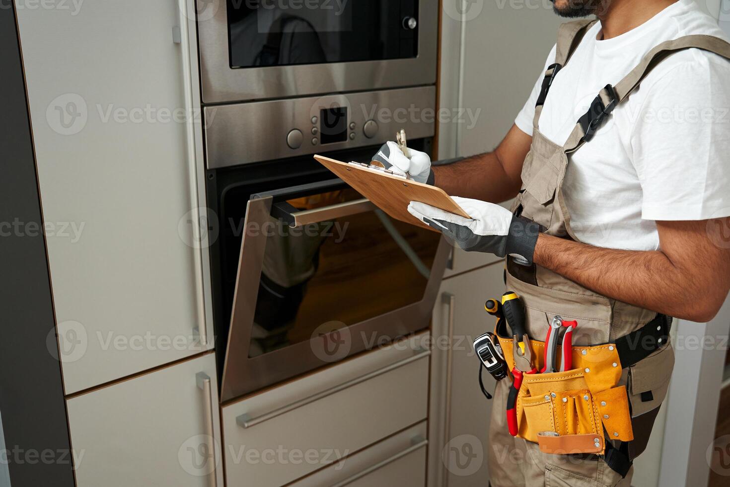 Close up of service worker in uniform standing near oven and writing on clipboard in kitchen photo