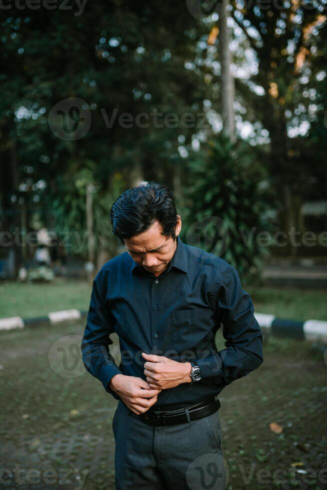 Formal asian man in park preparing for work attire buttoning shirt photo