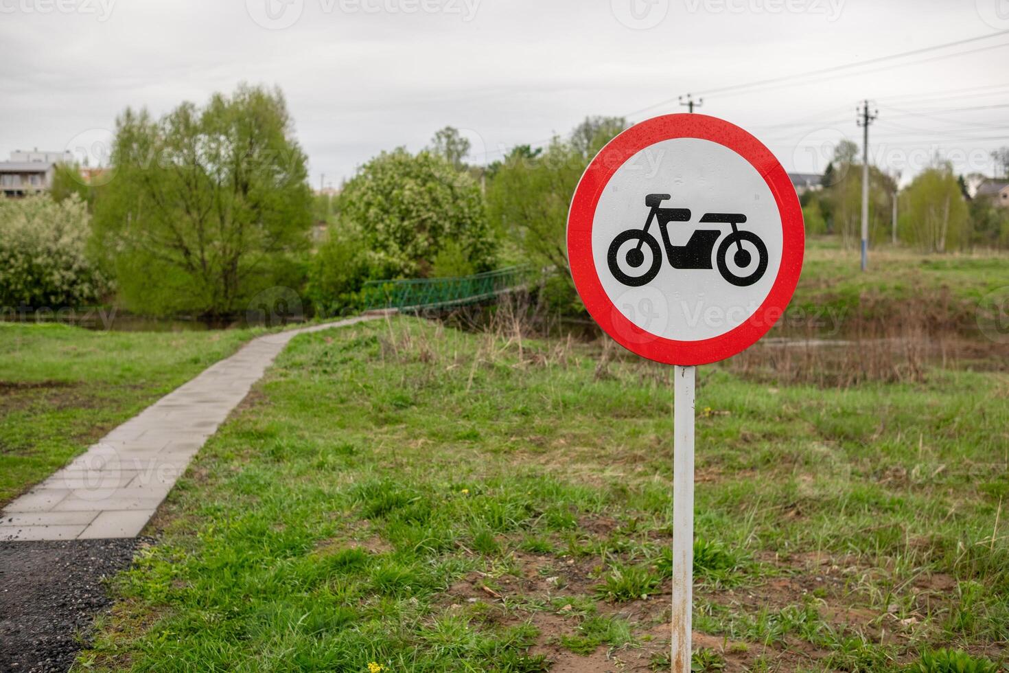 Motorcycle Prohibited Sign Near a Walking Path by a River in a Green Area on a Cloudy Day photo