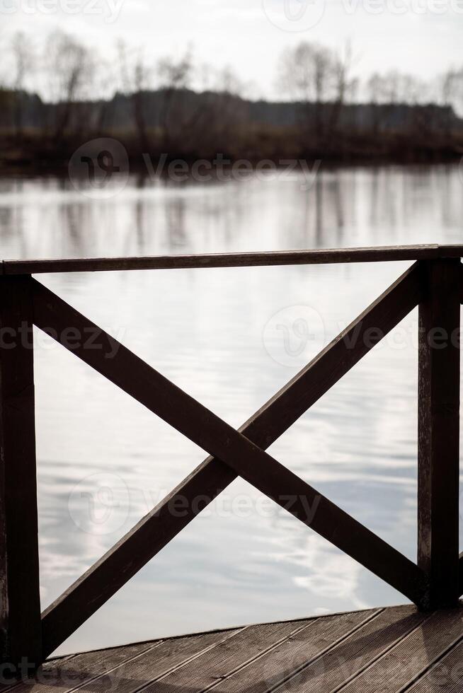 Wooden Railing Overlooking Calm Water Under Soft Cloudy Sky at Dawn photo