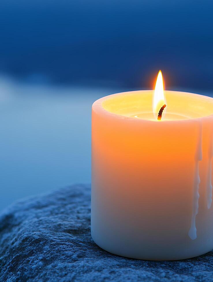 A close up of a lit candle on a textured surface with a blurred blue background in soft focus light photo