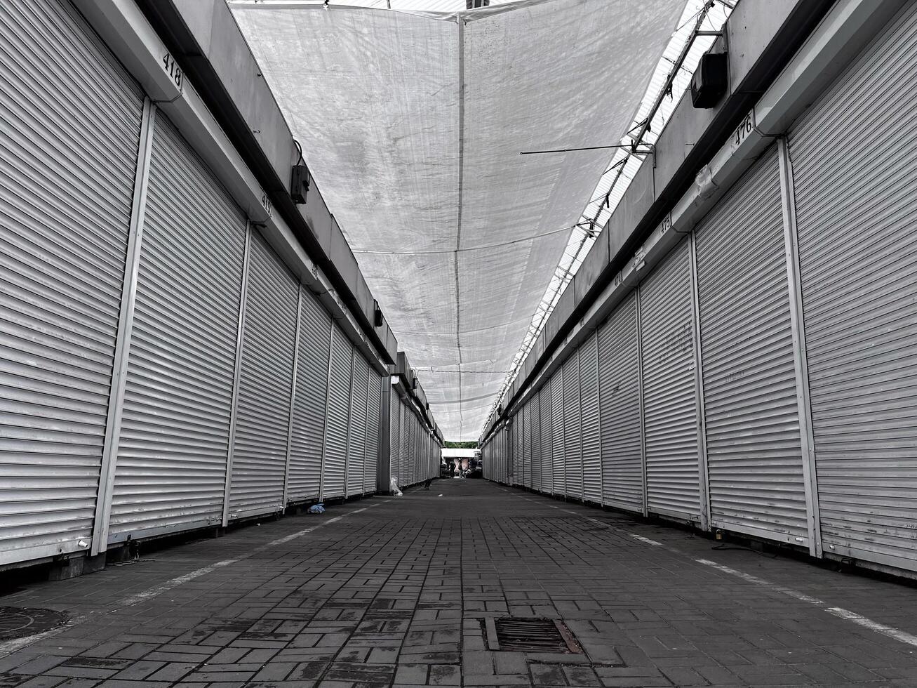 The empty market features countless closed stalls, their shutters down, as a soft light filters through the canopy above in the peaceful morning air photo