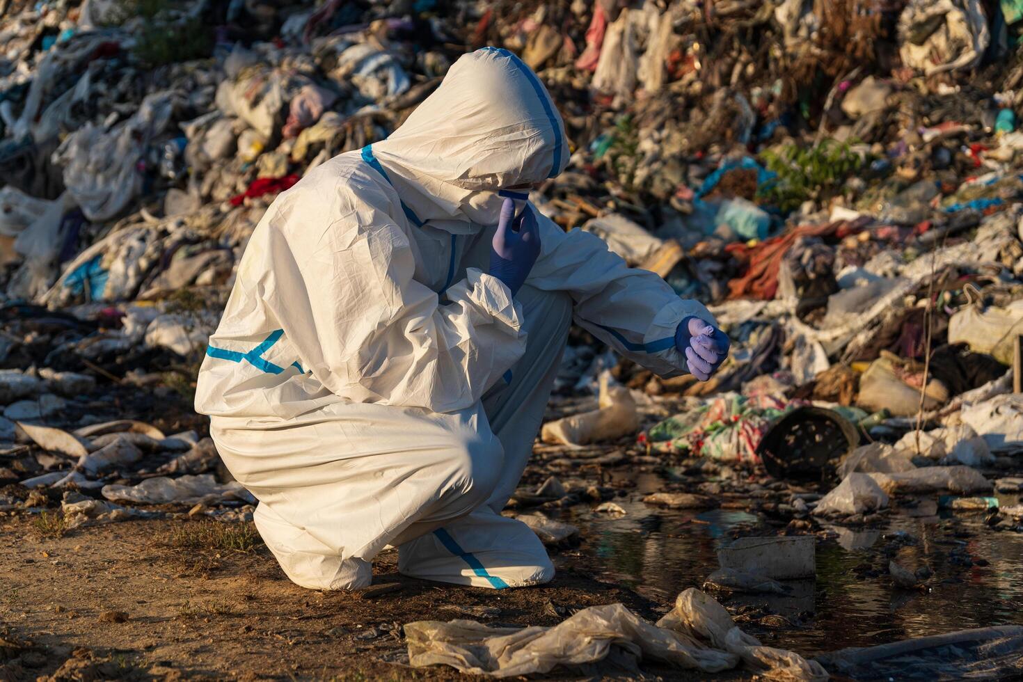Dressed in protective gear, a worker crouches at a landfill, analyzing waste amidst a backdrop of piled trash, shining in the soft morning light, addressing urgent environmental challenges photo