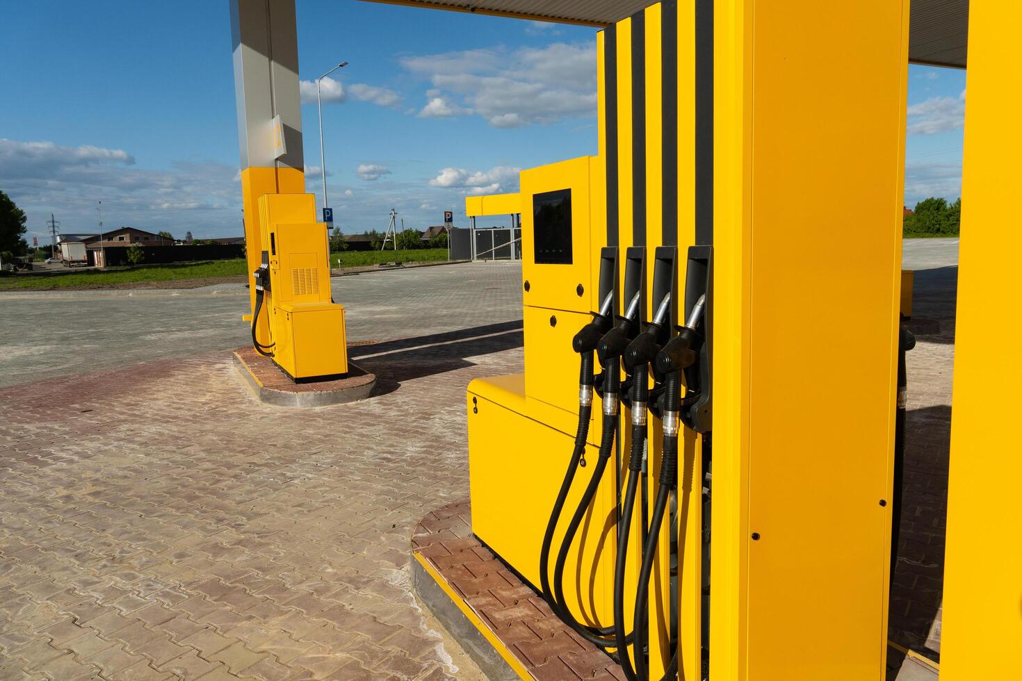 The fuel pumps, painted bright yellow, are situated at a deserted gas station under a clear blue sky, with lush green fields visible in the background on a sunny day photo