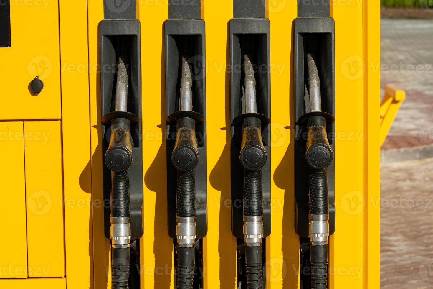 Four pump nozzles are lined up at a gasoline station, showcasing a bright yellow design against a clear daytime backdrop. The area is well-lit and inviting photo