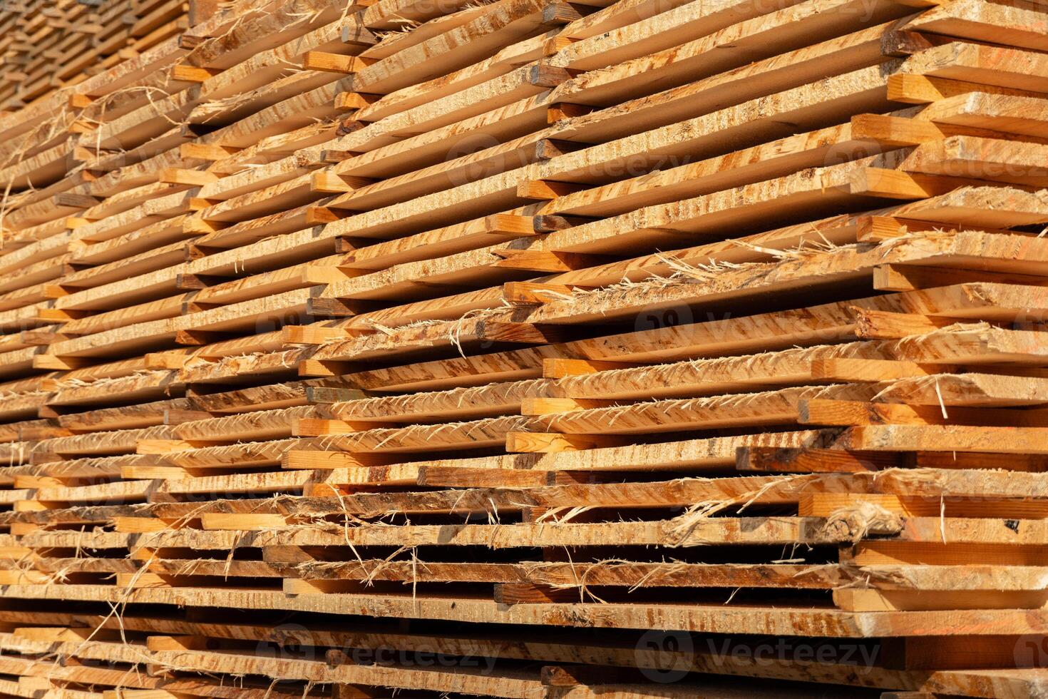 Wooden planks are neatly stacked, drying under sunlight at a lumberyard. The intricate grain patterns and textures of the wood are clearly visible, highlighting their natural beauty photo