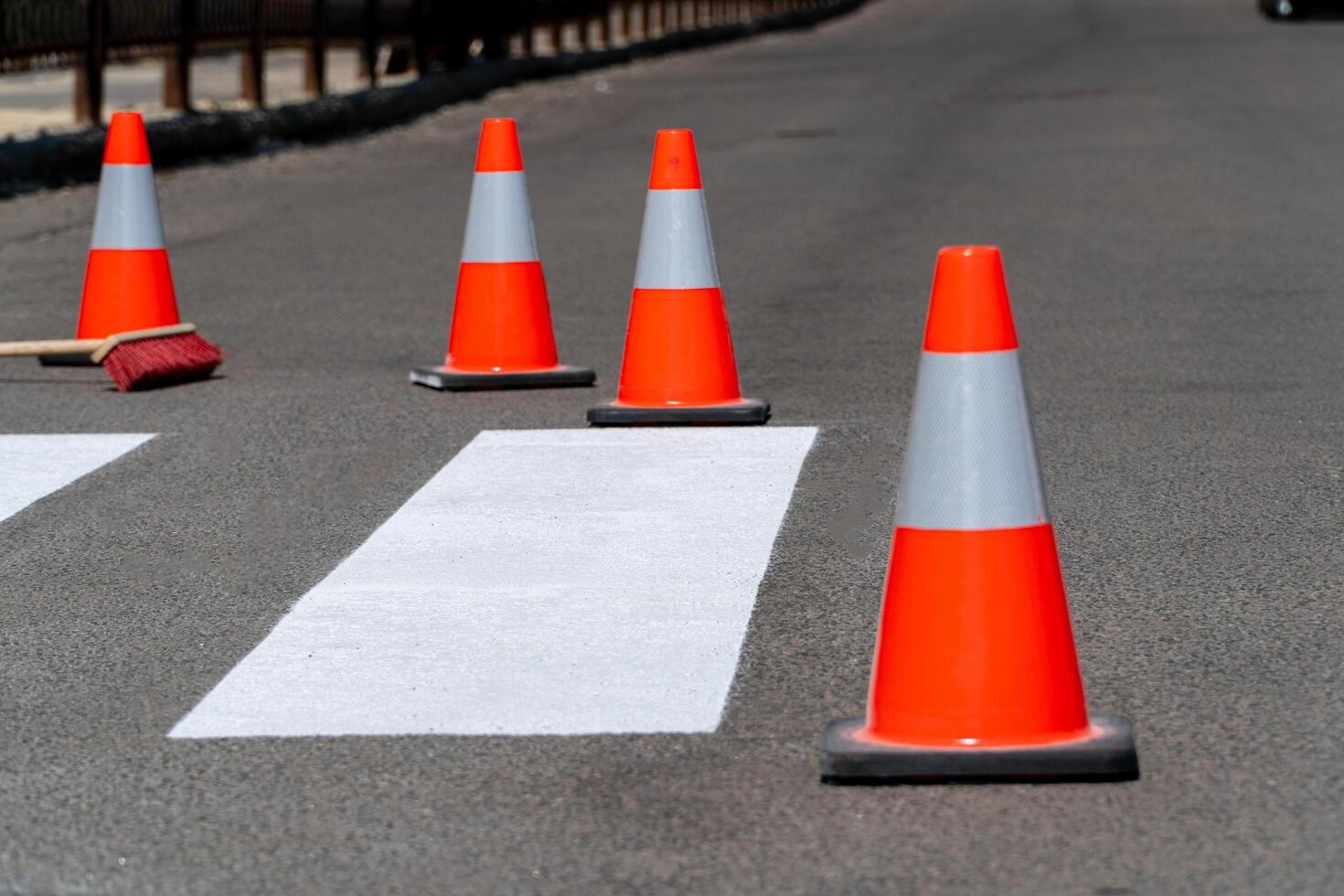 Bright orange traffic cones are placed along a newly marked crosswalk in an urban setting, directing pedestrians and ensuring safety in the area photo