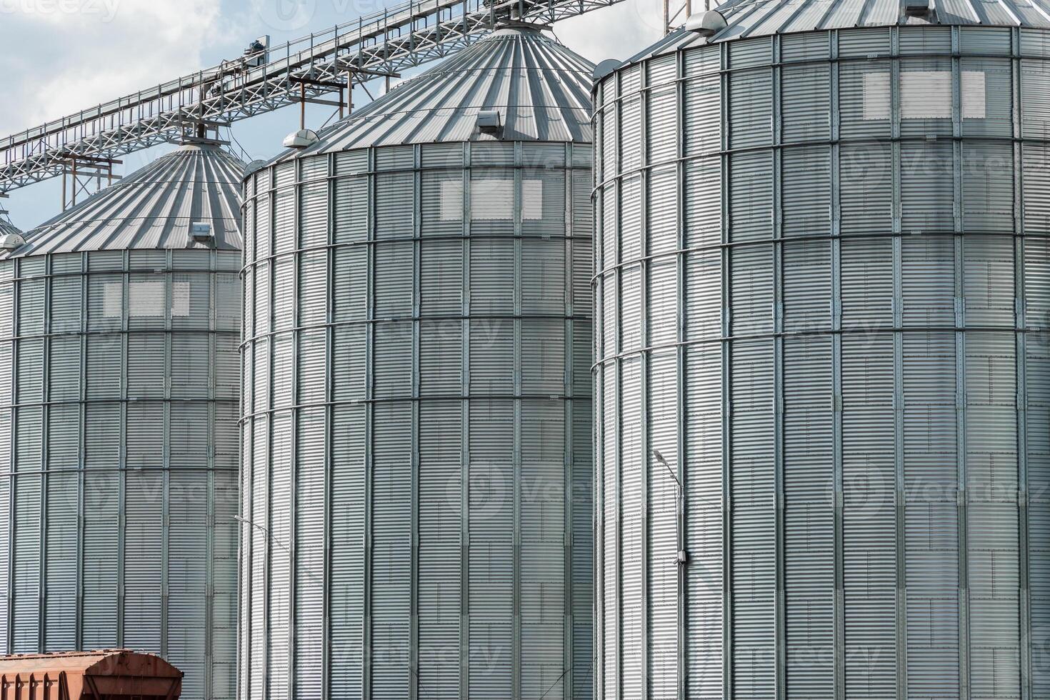 The view features several towering metallic grain silos set against a clear blue sky, highlighting their role in agricultural storage and production photo