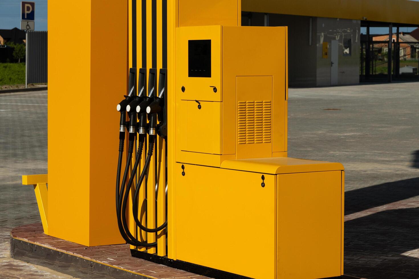 The fuel pump stands prominently at a gas station, featuring multiple dispensers with a striking yellow design, set against a clear blue sky and green surroundings photo