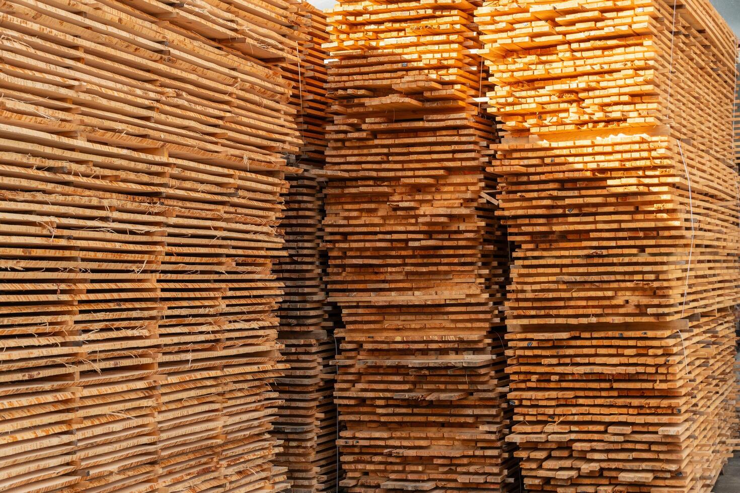 In a well-lit warehouse, numerous wooden planks are organized in neat stacks, highlighting a range of textures and shades. The arrangement emphasizes craftsmanship and storage photo
