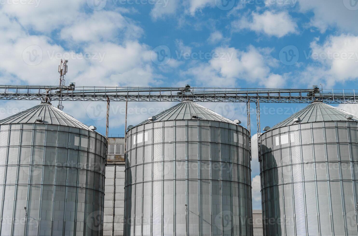 Tall metal silos are positioned against a backdrop of fluffy clouds, showcasing a modern agricultural setting that highlights food storage and production photo