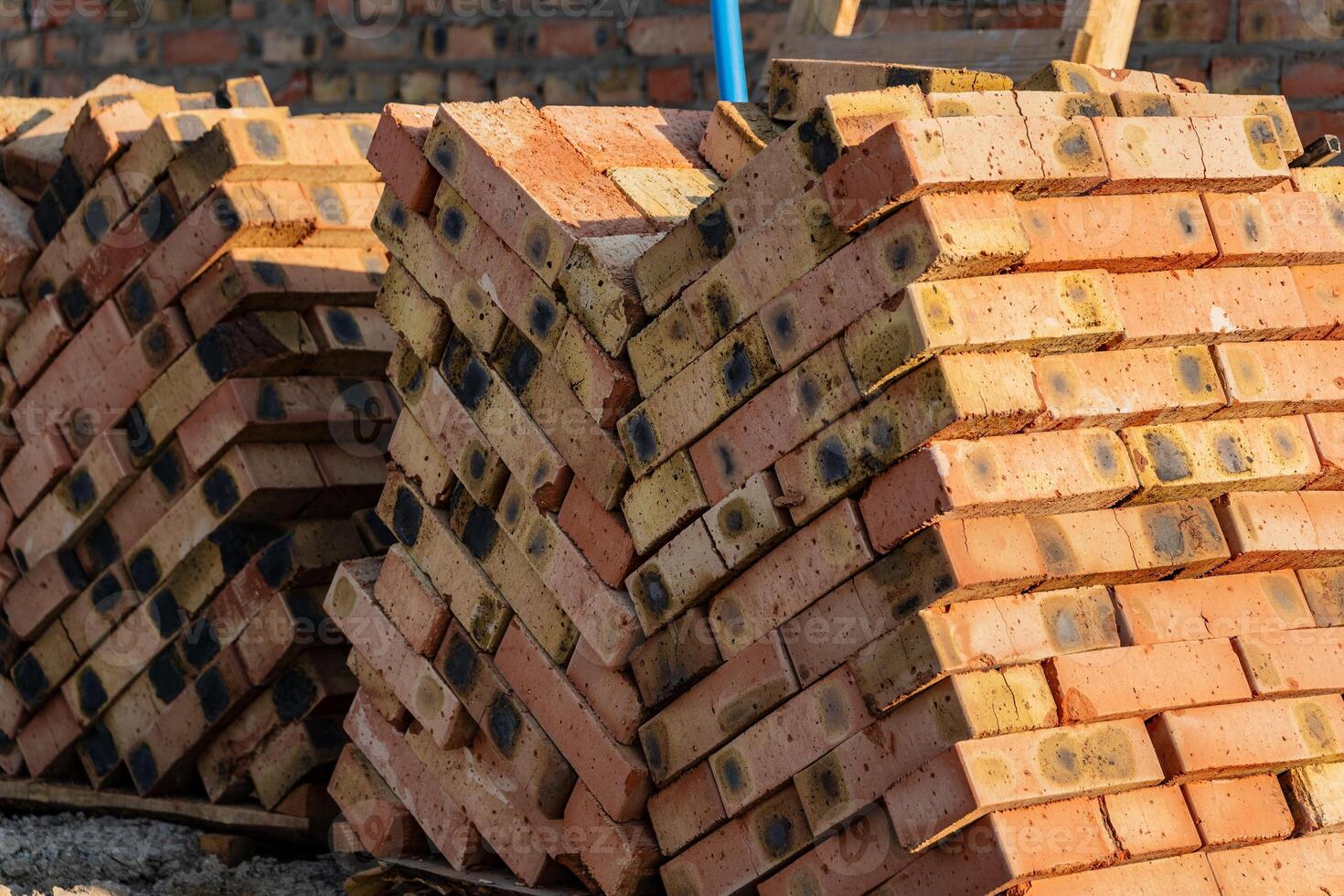 Piles of orange and brown bricks rest against a blurred backdrop at a construction site, suggesting preparation for upcoming building projects under bright sunlight photo