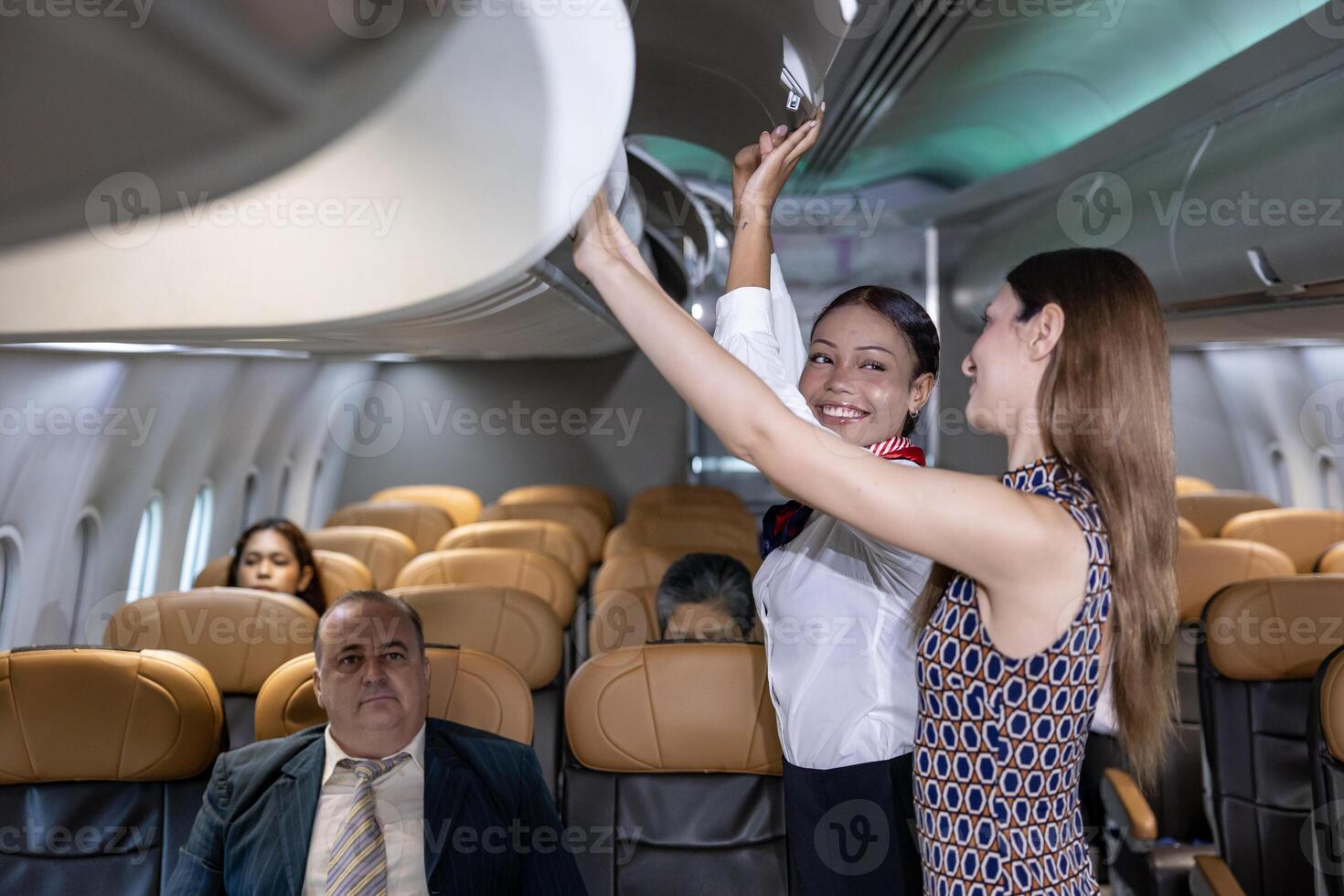 Flight attendant is helping passenger to put their bag into the overhead luggage compartment lid for carry on after seated and preparing to take off photo