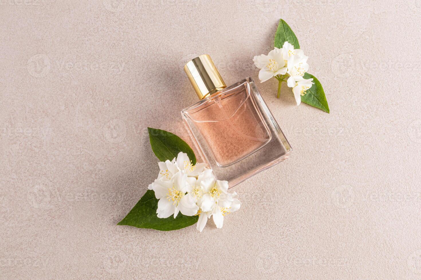 A chic bottle with a gold cap lies on a beige stone background with delicate white jasmine flowers. A blank mockup. Product presentation photo