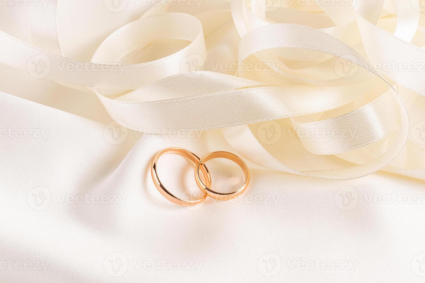Two gold wedding rings lie on an satin fabric with beautiful cream colored ribbons. Front view. Wedding Mockup for Card Design, Invitation. photo