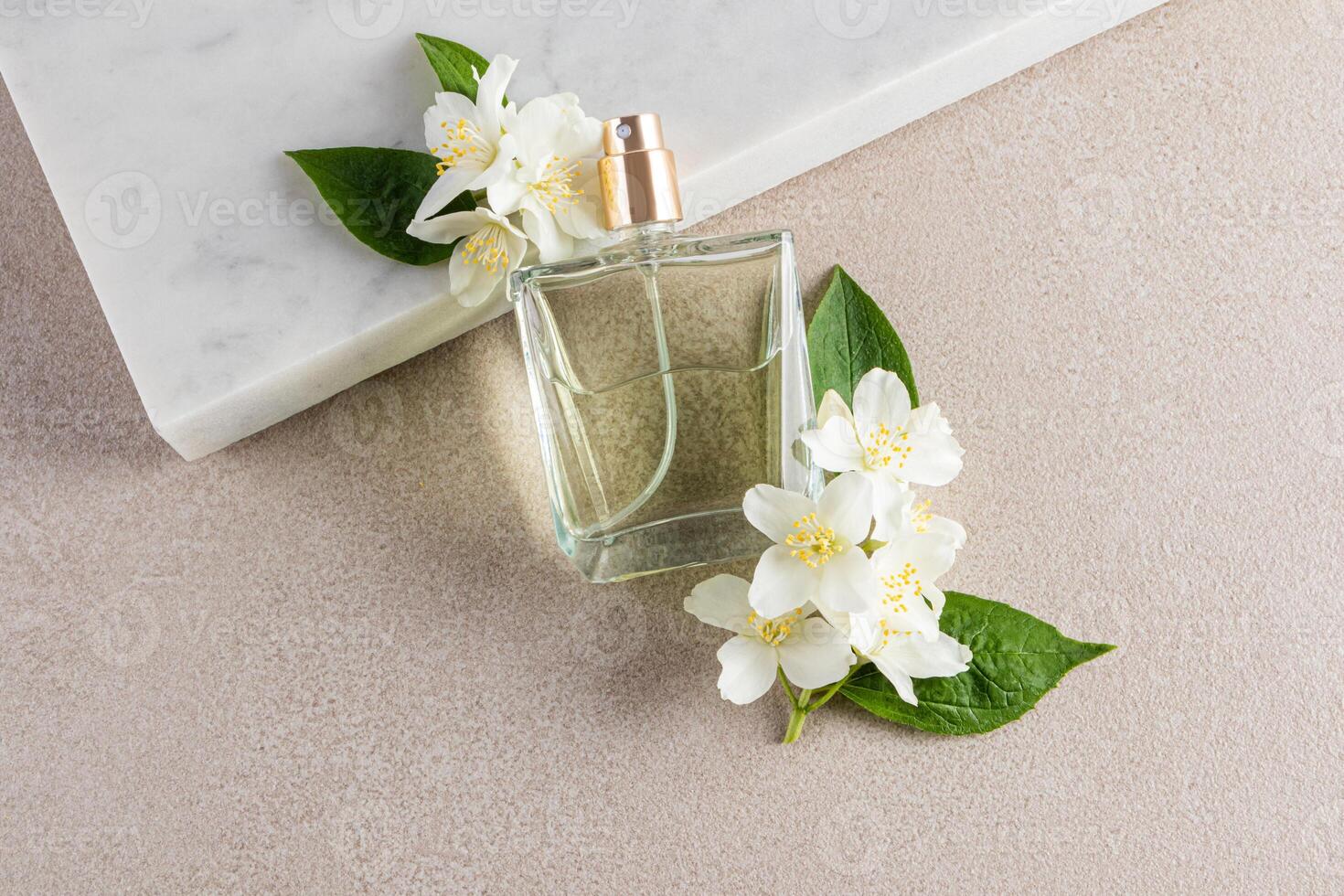 An elegant perfume bottle leans on a white marble podium with jasmine flowers. A blank bottle mockup. Fragrance presentation. beige stone background. photo