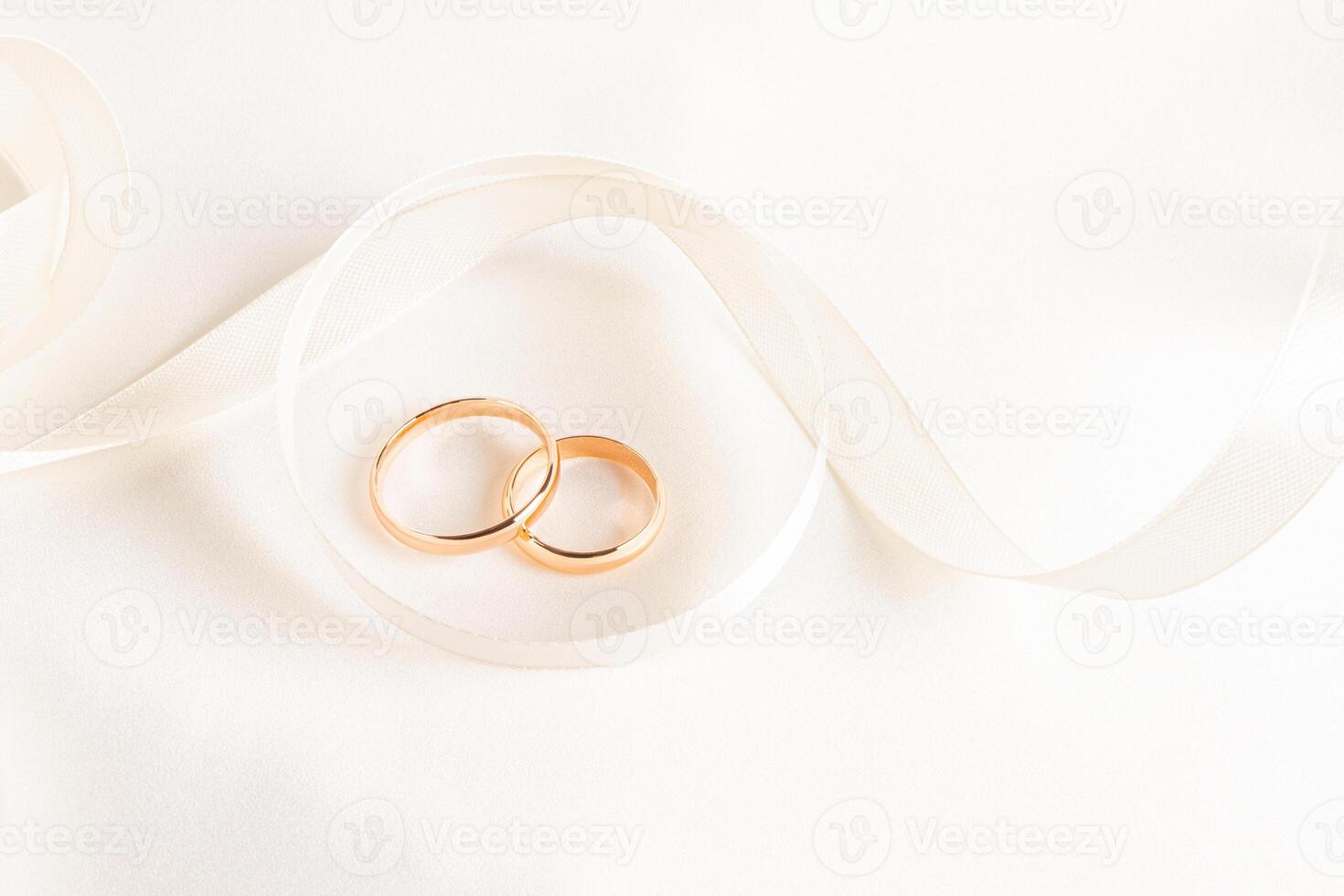 Two gold wedding rings lie inside a beautifully twisted beige ribbon on a satin background. top view. A copy space. presentation of wedding rings photo