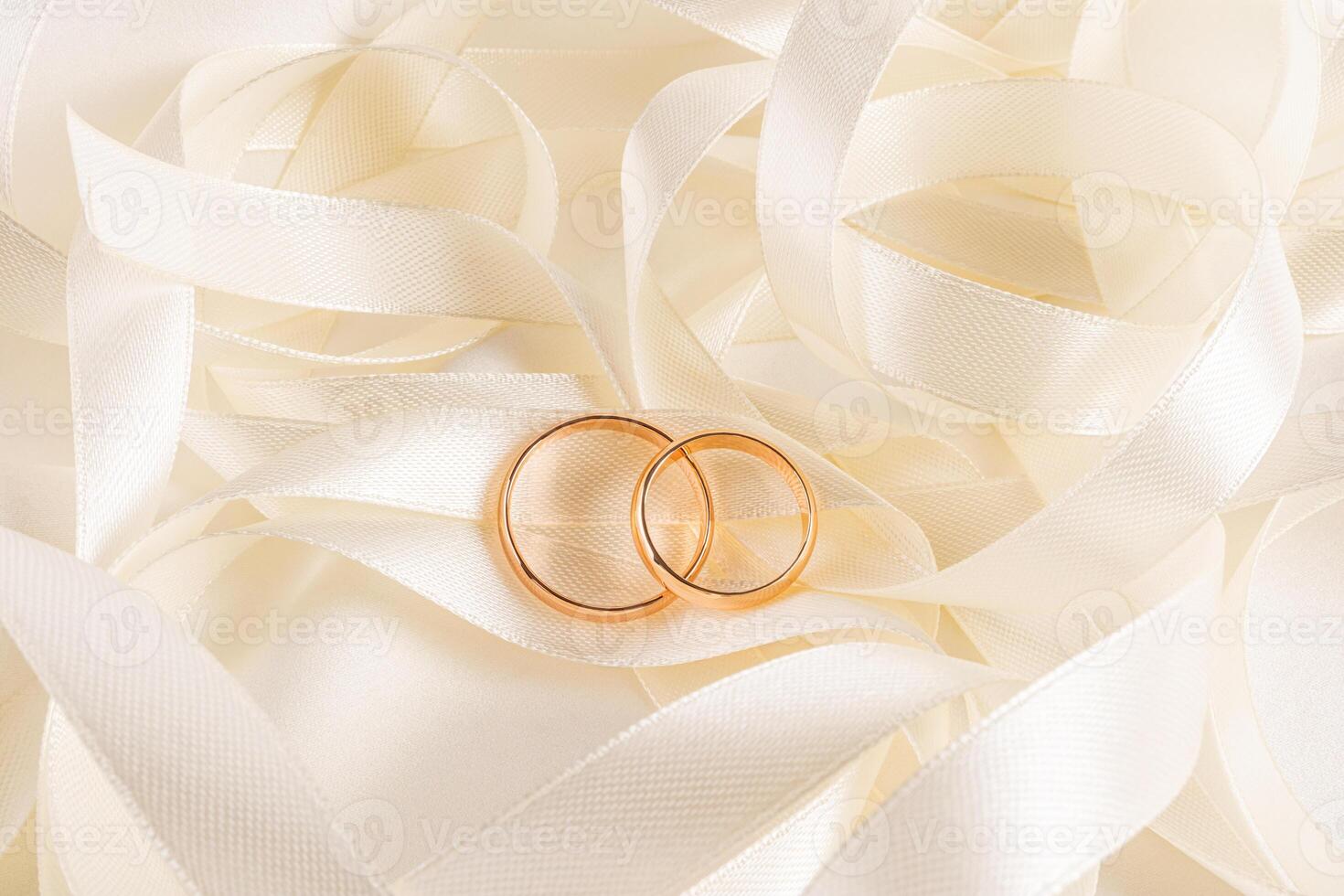 Top view of two gold wedding rings lying on a beige pile of satin ribbons. A copy of the space. Wedding mockup for card design, invitation. photo