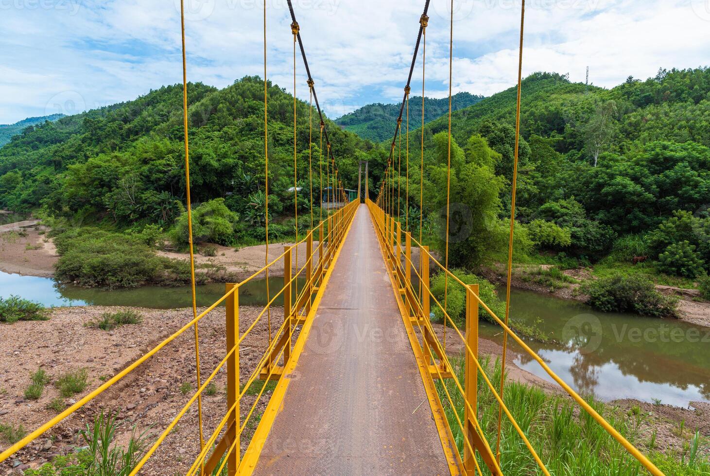 Yellow Traditional Iron Pedestrian Bridge Across Mountain River Against Mountain Backdrop In Vietnam photo