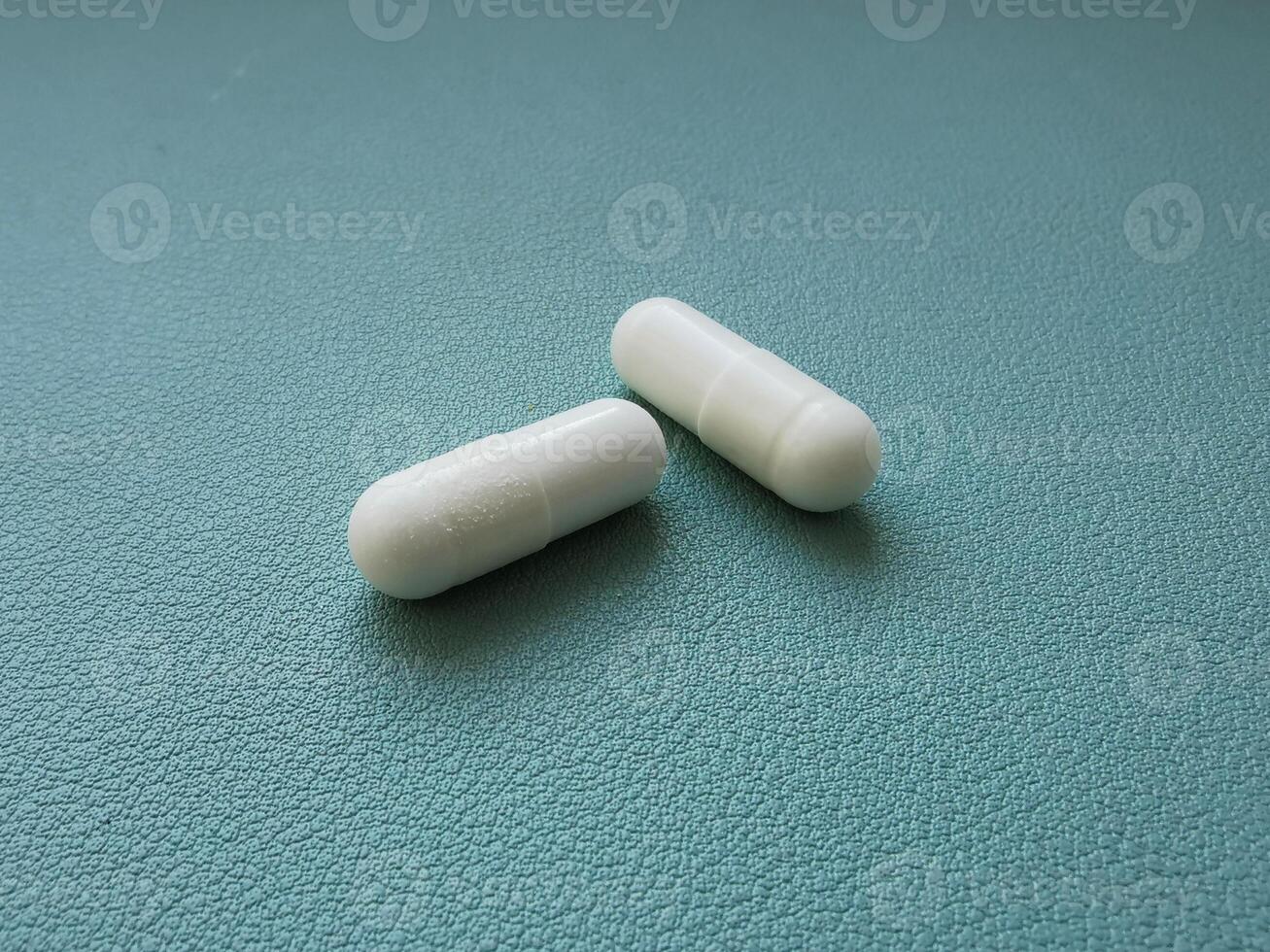 Two white medical pills on green background with space photo