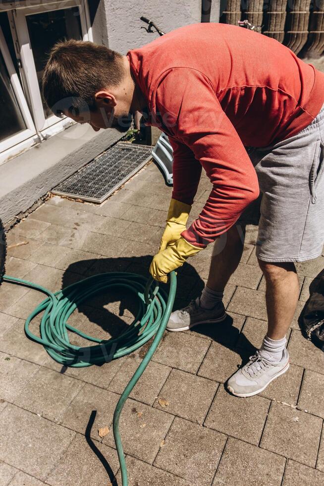 Man winding green garden hose preparing for watering plants outdoors summer gardening tool nature care photo