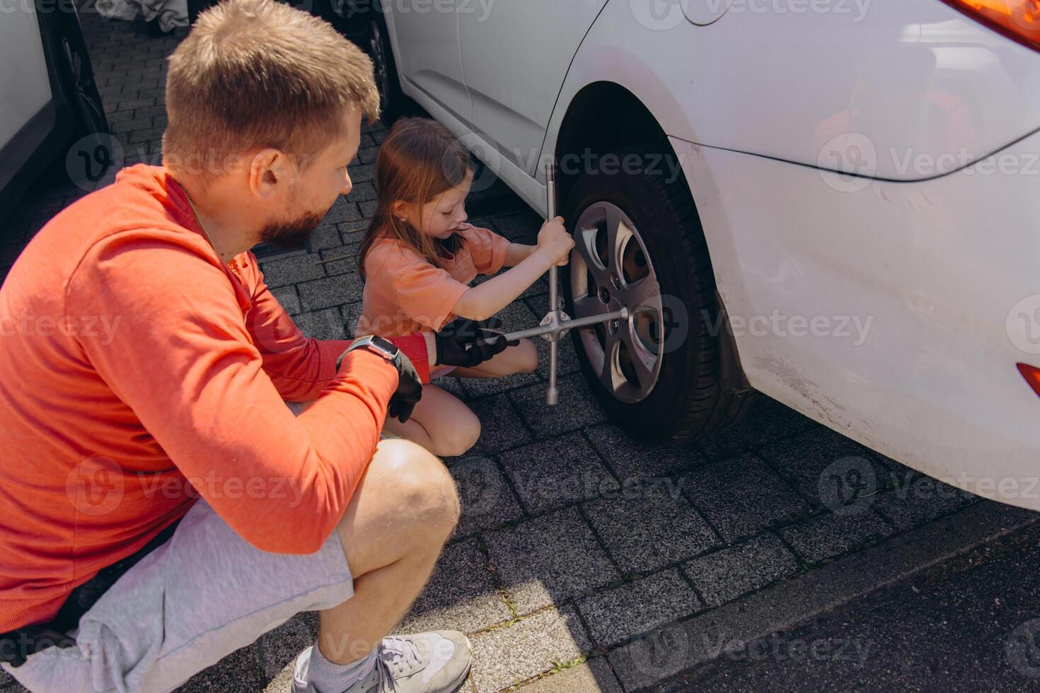 little girl assists her father in changing the car tires,creating heartfelt and bonding experience photo