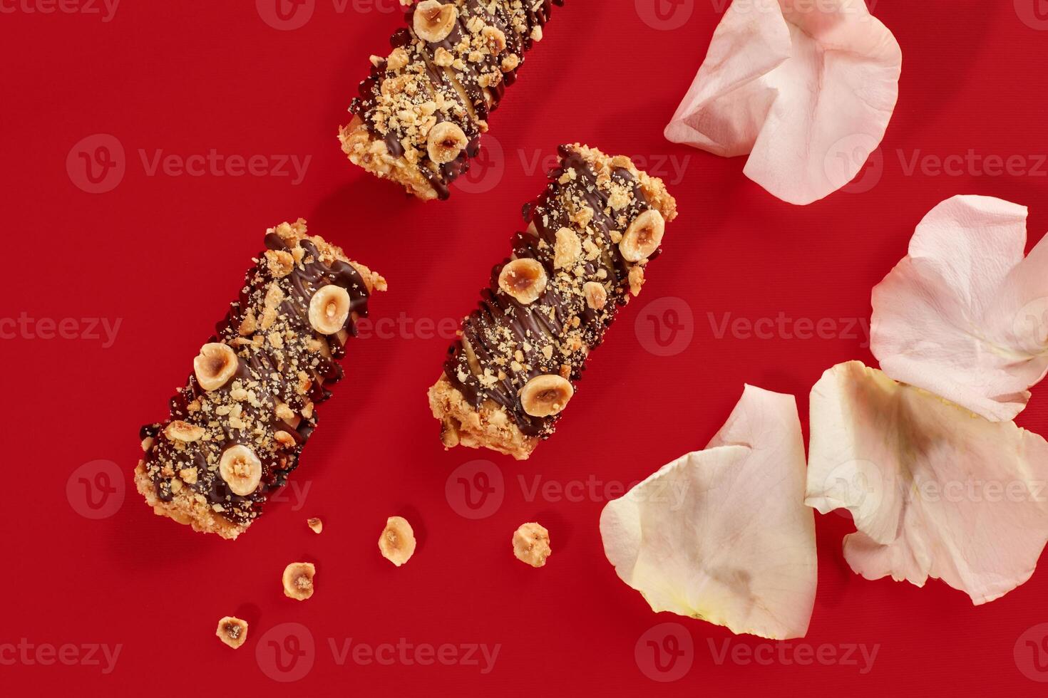 Delicious hazelnut cakes with chocolate and rose petals on red background photo